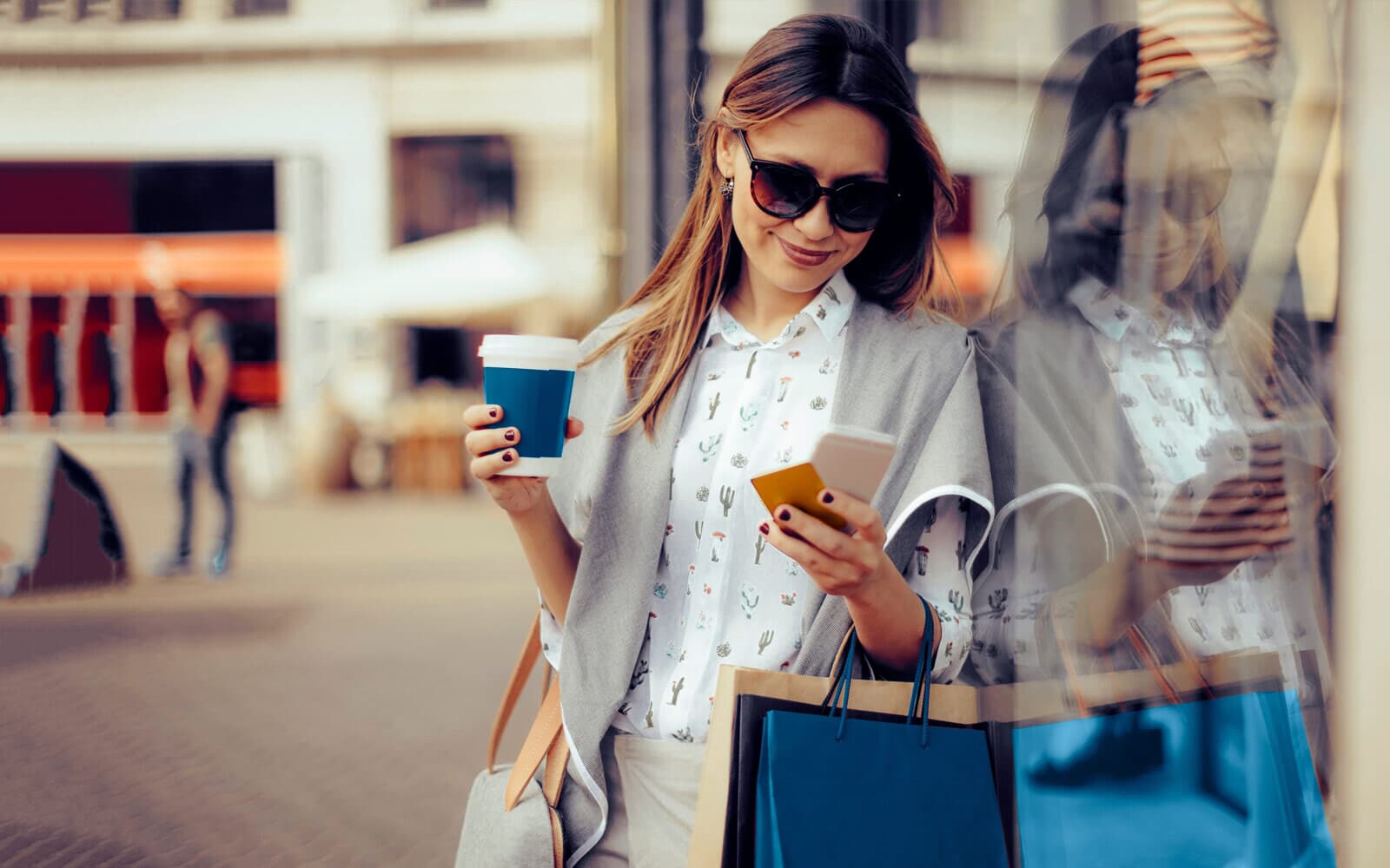 Woman on her phone, holding a to-go cup of coffee and shopping bags