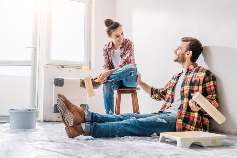 Couple sitting in their home with paint rollers