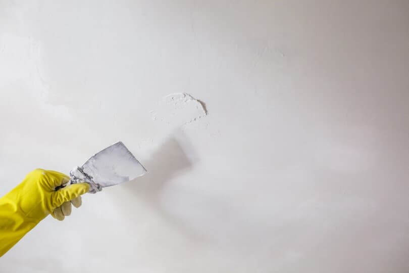 Hand in a yellow glove applying putty to a hole in the wall
