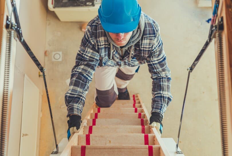 Man climbing a ladder into an attic wearing a hard hat