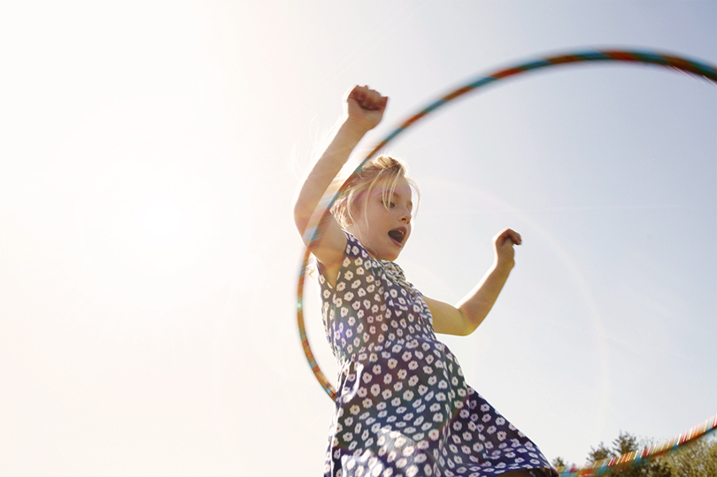 A young girl playing with a hula hoop outside