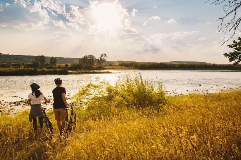 Couple riding bikes by water near Cranstons Riverstone in Calgary AB