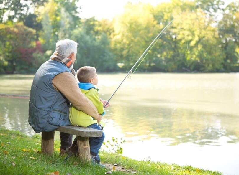 Grandfather and grandson fishing at the edge of a lake