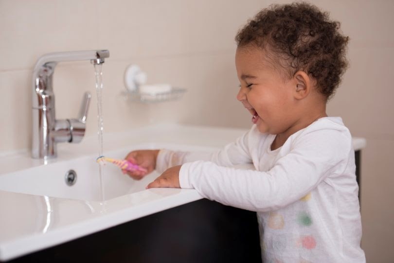 Child gleefully washing toothbrush under running water concept