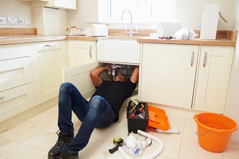 Man lying on his back working on the pipes under a sink with tools next to him on the floor