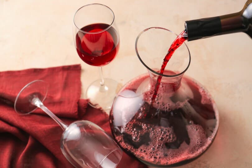 Pouring of wine from bottle into decanter on table