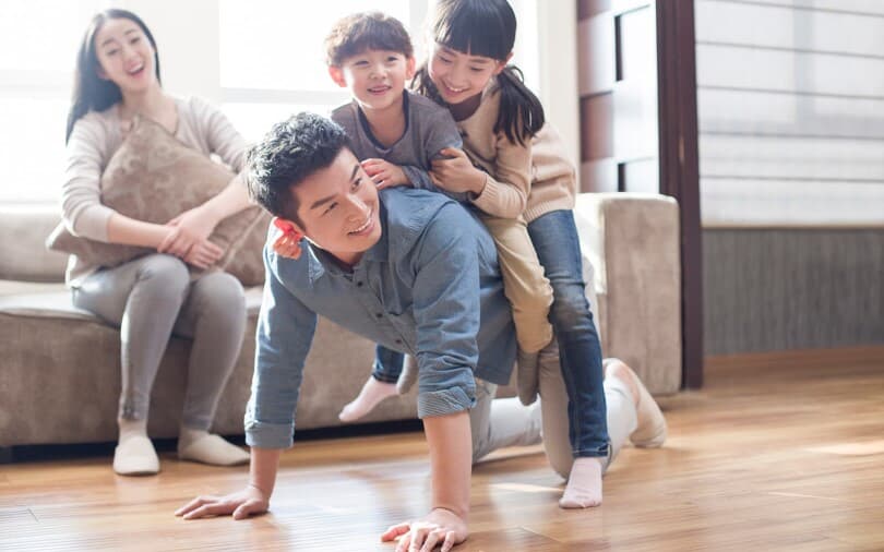 Kids crawling on their dad's back while mom looks on laughing