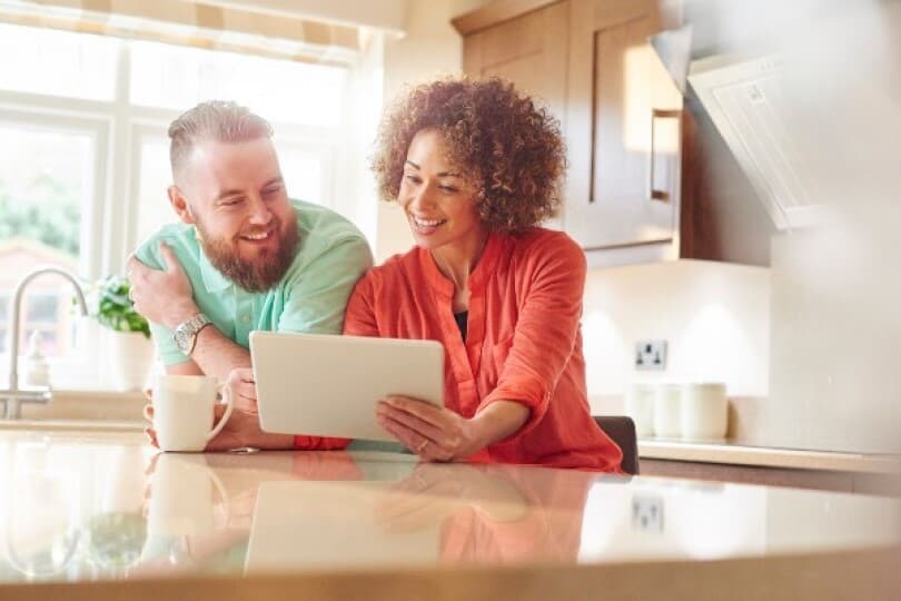 Couple sits in kitchen and reviews home wish list on a tablet