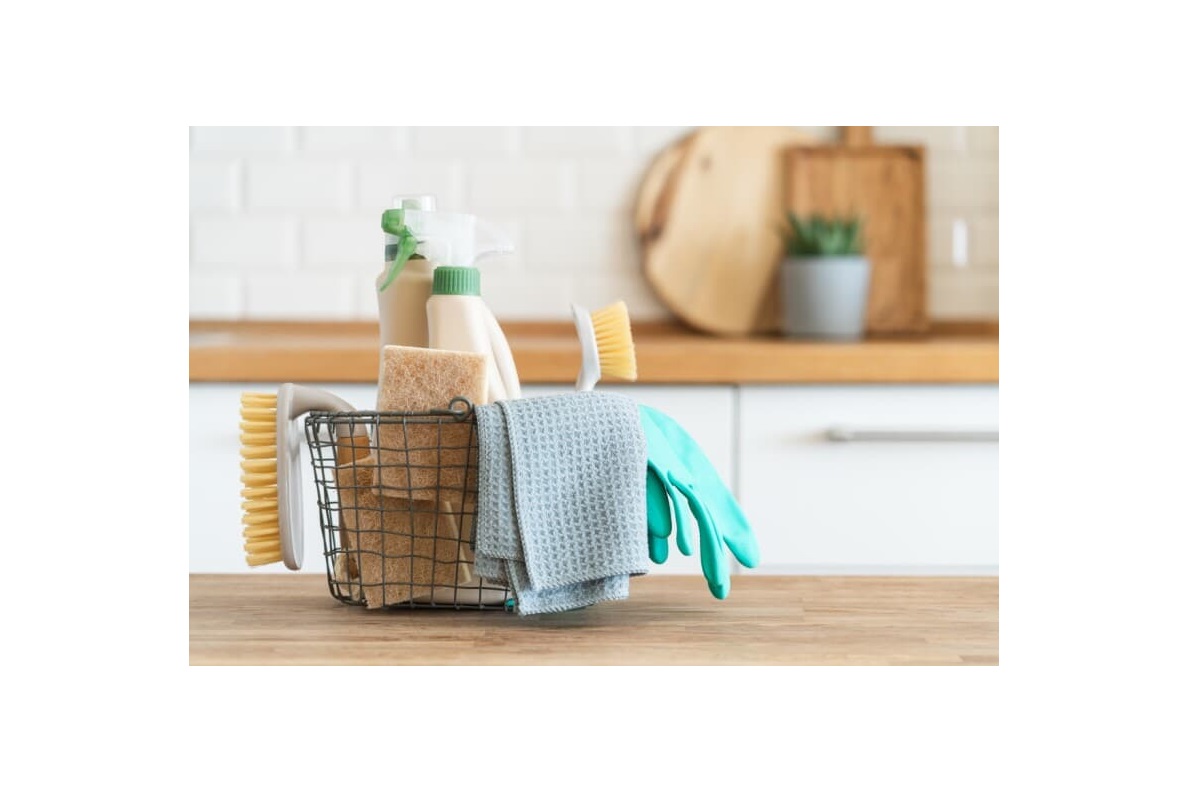 Basket with brushes, rags, natural sponges and cleaning products and modern kitchen interior in the background
