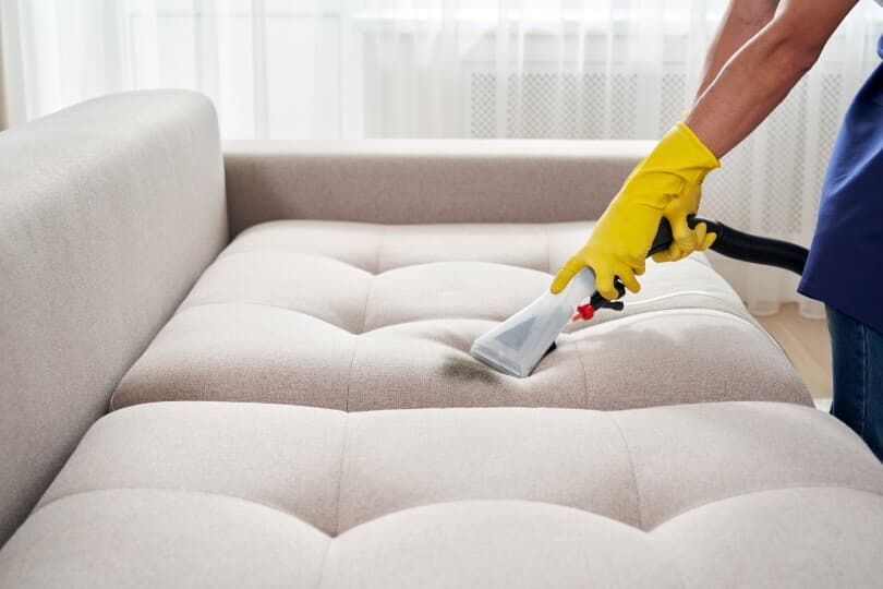 Hands deep cleaning a couch cushion with a vacuum attachment