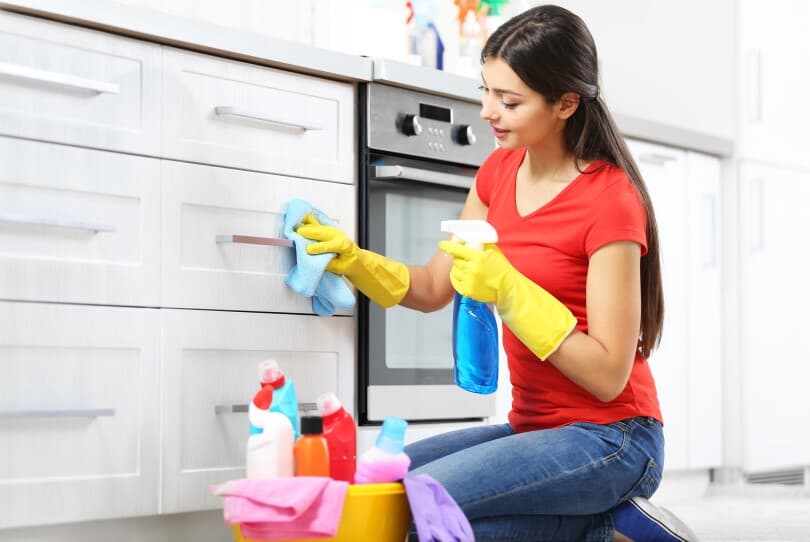 Woman kneeling in a kitchen disinfecting cabinet pulls