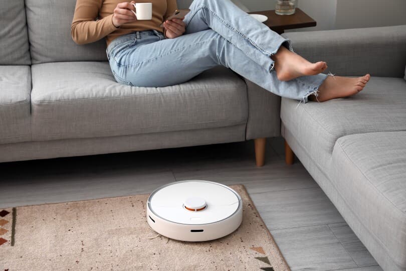 Woman lounging on a couch with coffee while a robotic vacuum runs