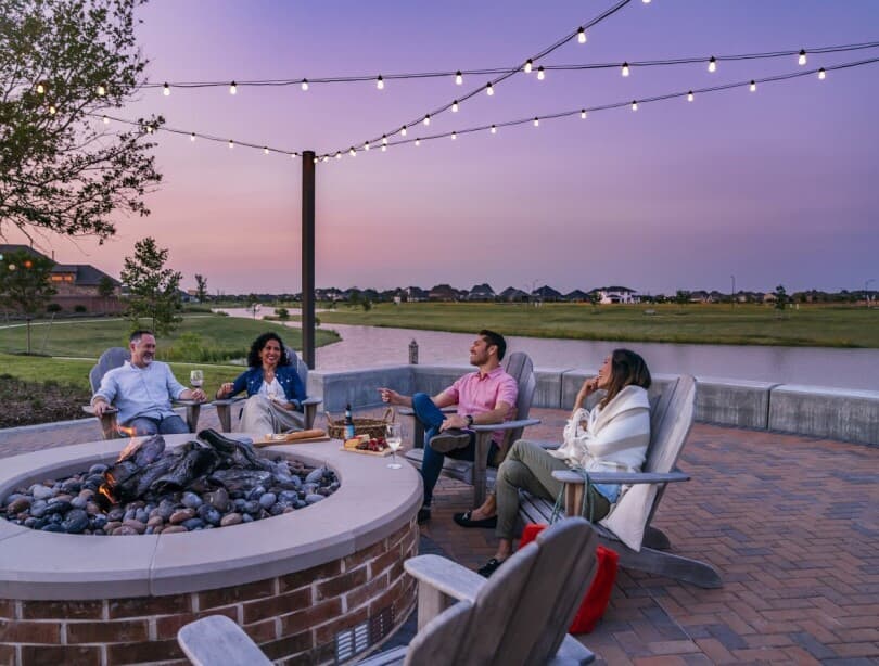 Group of friends around an outdoor fire pit at sunset enjoying wine and beer