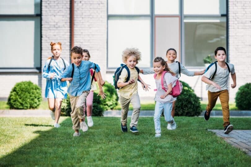 Kids running with backpacks in front of a school