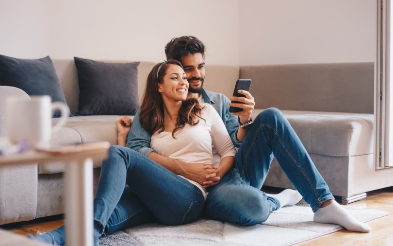 Young couple snuggled in front of a couch looking at a phone