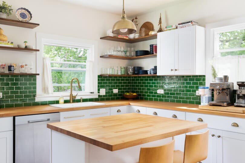 Kitchen with white cabinets, a natural wood countertop, green subway backsplash, and a gold pendant light