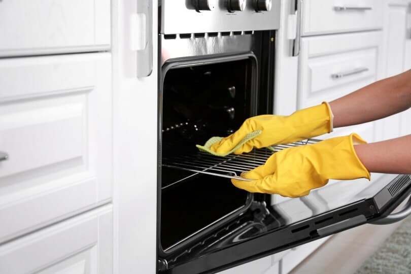 Hands with yellow gloves cleaning an oven