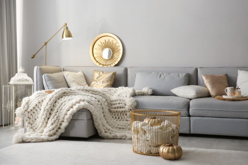 Gray couch with gold accents and white chunky knit blanket