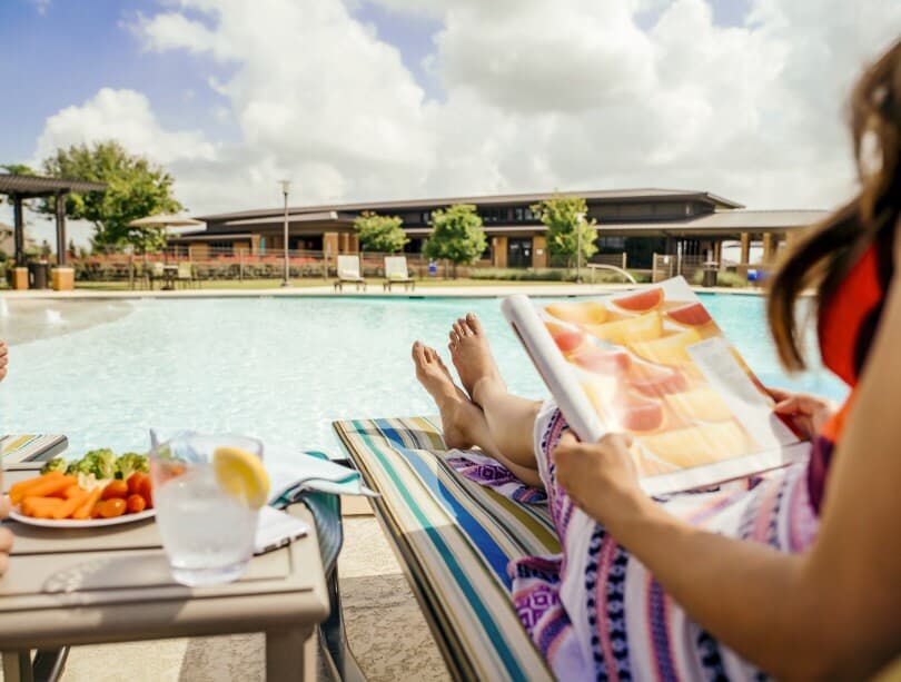 Woman lounging poolside with snacks and a magazine at Elyson by Brookfield Residential in Katy TX